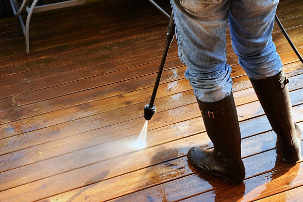 Worker pressure washing a wooden deck to remove dirt and grime. -deck cleaning services