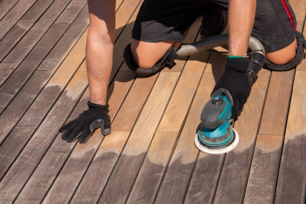 Worker sanding wooden deck surface with electric sander for restoration. -deck cleaning services